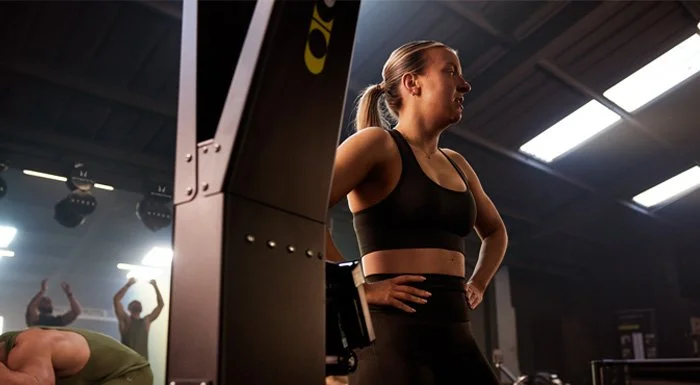 Woman in a black sports bra and leggings resting between sets in the gym