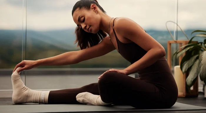 Woman in black activewear stretching her hamstrings on a yoga mat at home