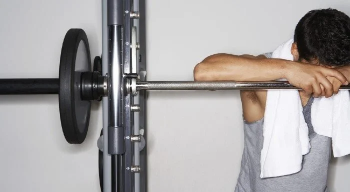 Tired man resting his head on a barbell in a squat rack
