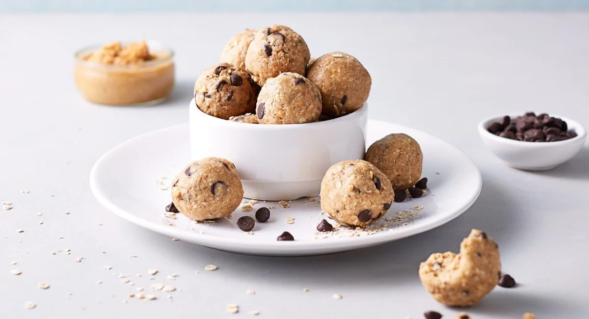 Homemade protein balls in a bowl on a plate, with chocolate chips and nut butter on the side