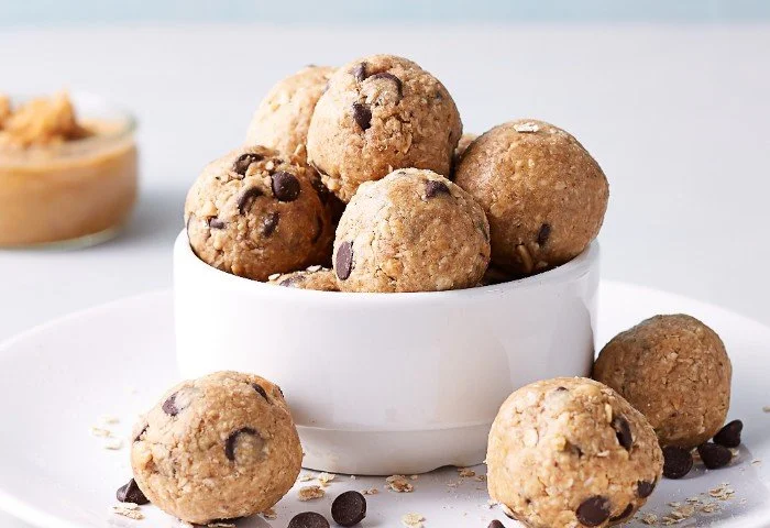 Chocolate chip protein balls in a white bowl, with nut butter in the background