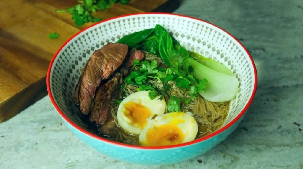 Bowl of beef ramen with sliced steak, soft-boiled eggs and pak choi