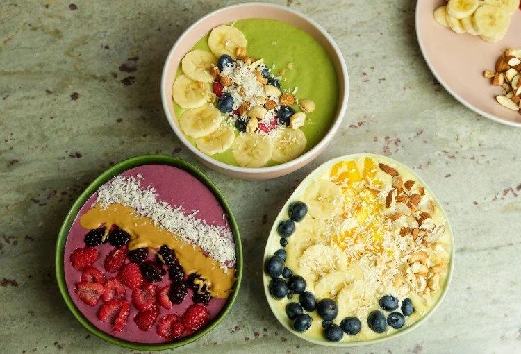 Three smoothie bowls topped with fruit, coconut and nuts
