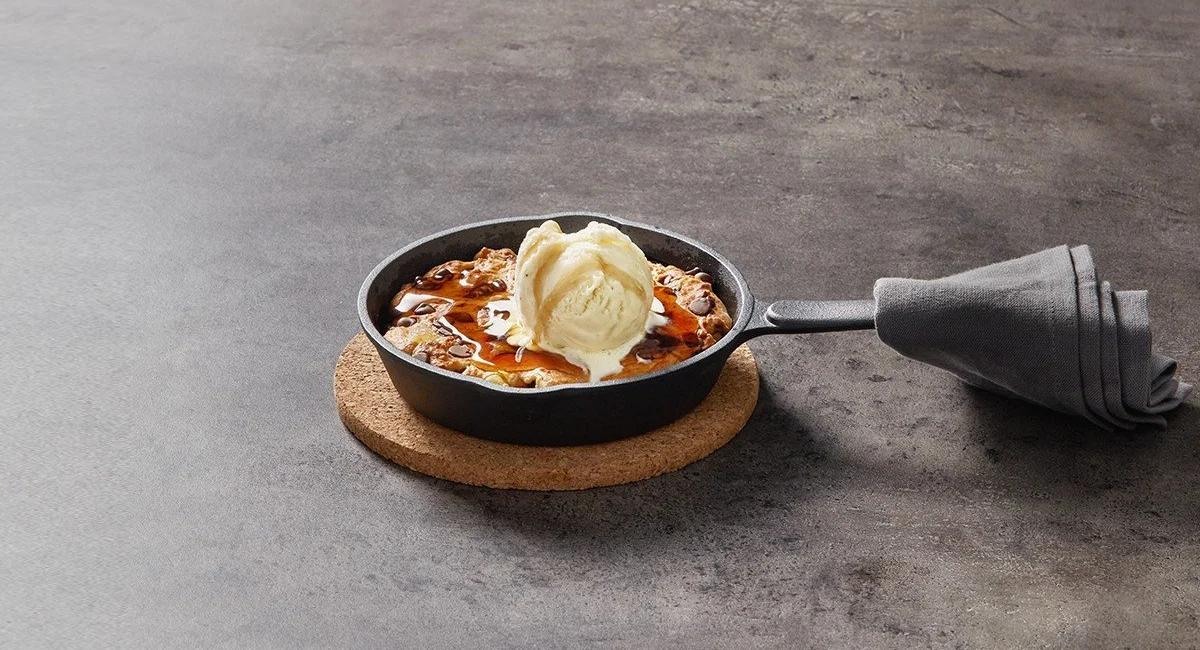 Skillet of protein cookie dough topped with ice cream and syrup