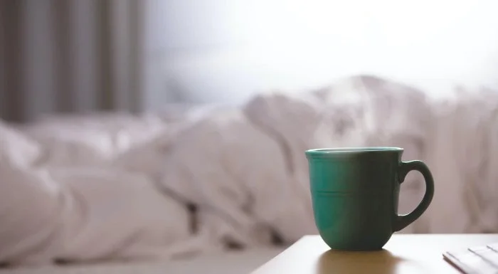 Mug on a bedside table next to an unmade bed