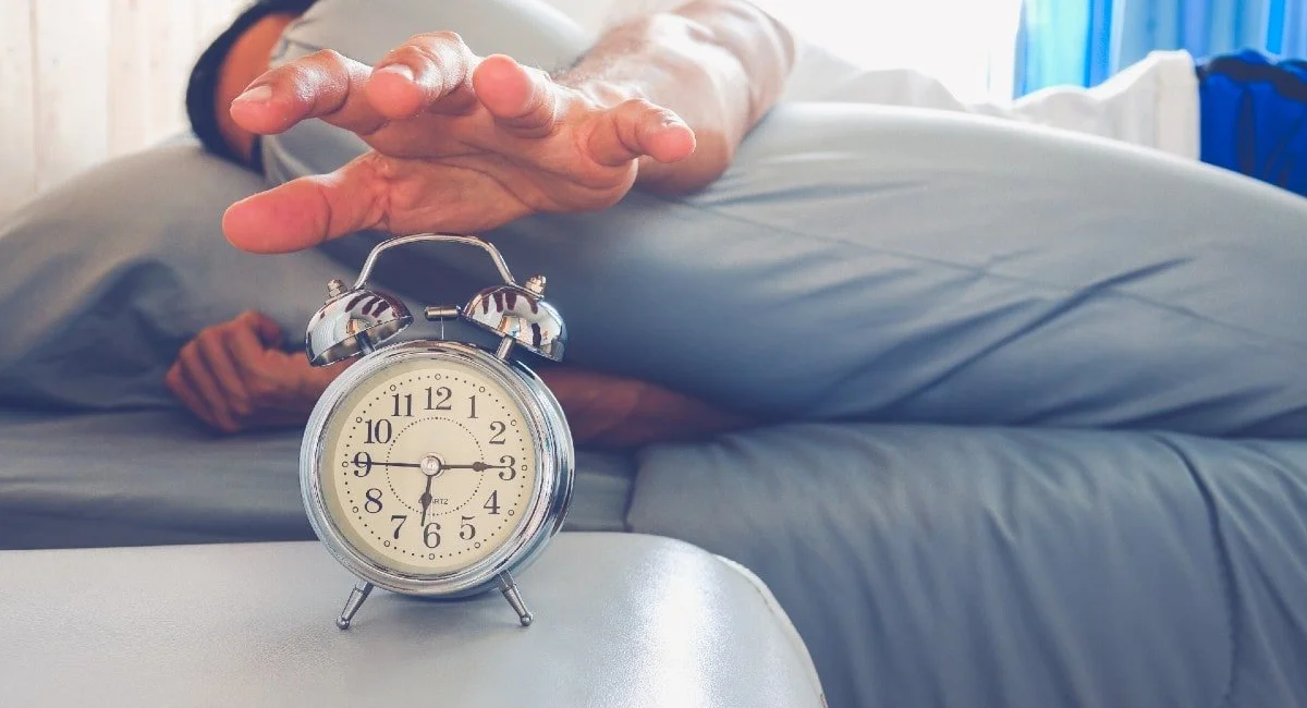 Hand reaching out from bed to turn off an alarm clock