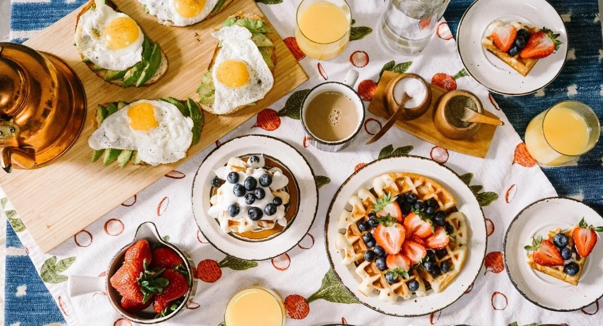 Breakfast table spread with eggs on toast, waffles, fruit and juice