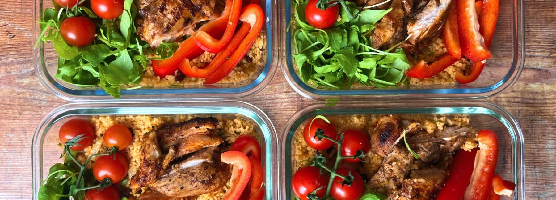 Four meal prep containers of harissa chicken with couscous, tomatoes and peppers