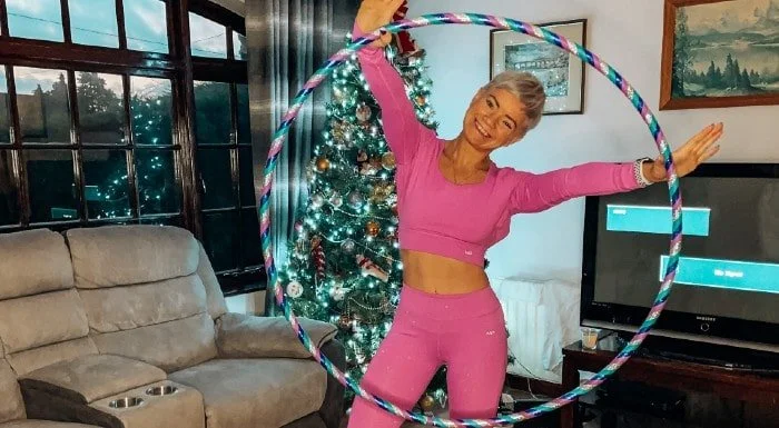Woman hula hooping in her living room next to a Christmas tree