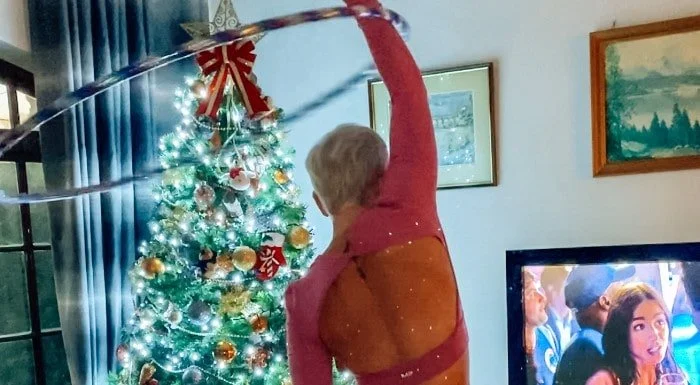 Woman hula hooping next to a Christmas tree, seen from behind
