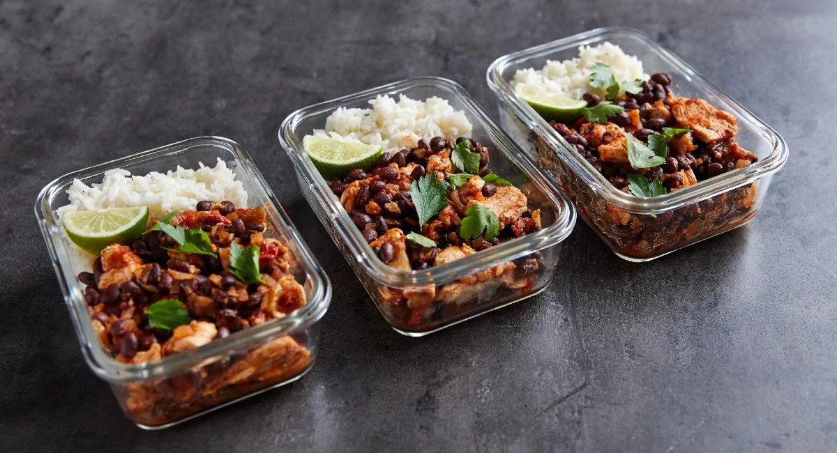 Three meal prep containers of chicken burrito bowl with rice, black beans and lime