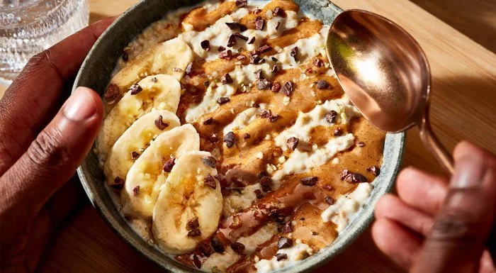 Bowl of porridge topped with banana, cacao nibs and nut butter