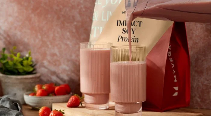 Strawberry shake being poured into glasses next to a pouch of Myvegan Impact Soy Protein