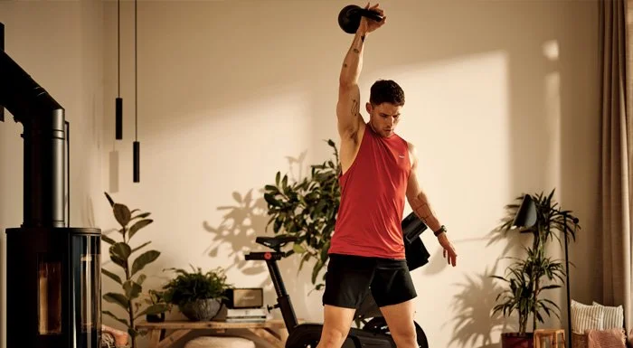 A man lifting a kettlebell over his head during a home workout.