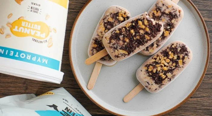 Peanut butter ice cream lollies on a plate, next to a tub of Myprotein Peanut Butter