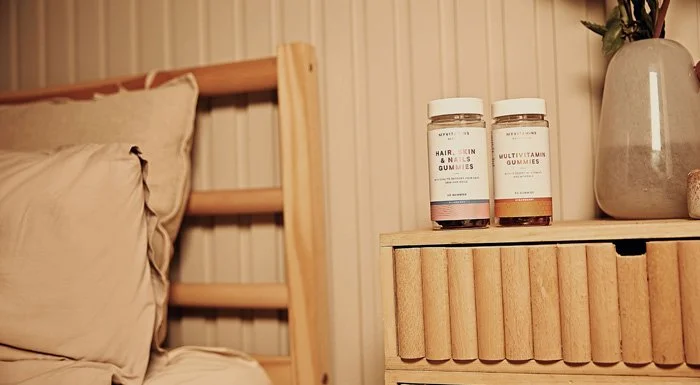 Two tubs of Myprotein vitamin gummies on a bedside table