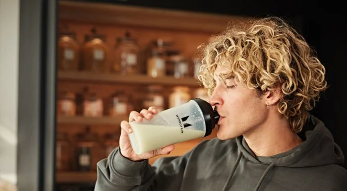 Man with curly hair drinking a protein shake from a Myprotein shaker