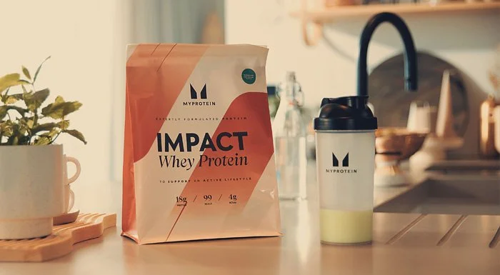 Myprotein Impact Whey Protein pouch next to a shaker on a kitchen counter