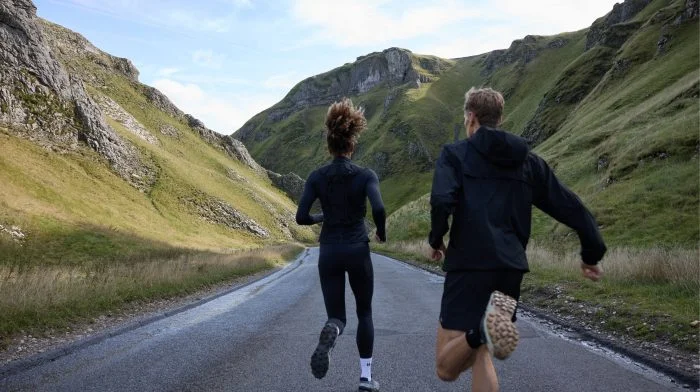 Man and woman running along a road through a green valley