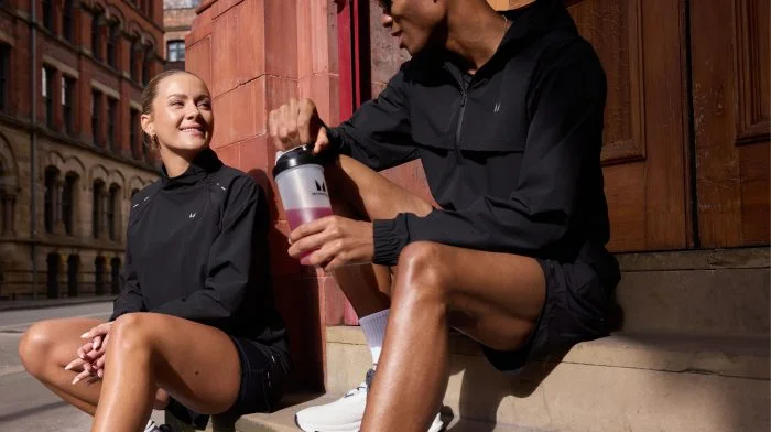 Man and woman resting on steps after a run, one holding a Myprotein shaker