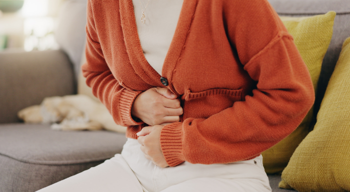 Woman in an orange cardigan holding her stomach