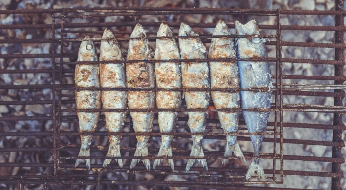 Row of sardines cooking on a grill