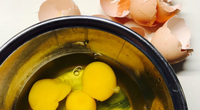 Cracked eggs in a mixing bowl with the shells beside it