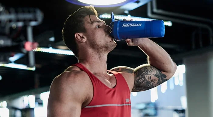 Man drinking from a blue Myprotein shaker in the gym