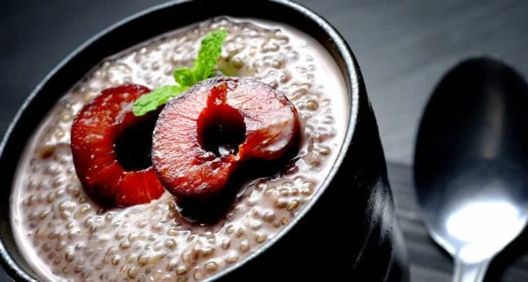 Chia seed pudding topped with cherries and mint in a black bowl