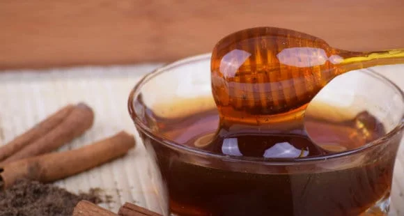 Honey dipper over a glass bowl of agave syrup, with cinnamon sticks