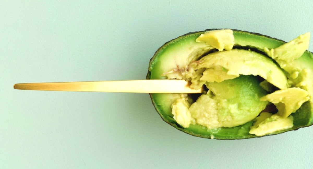 Spoon scooping flesh from a halved avocado