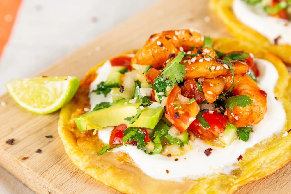 Tortilla stacked with sour cream, chipotle prawns, avocado and tomatoes to make a prawn taco.