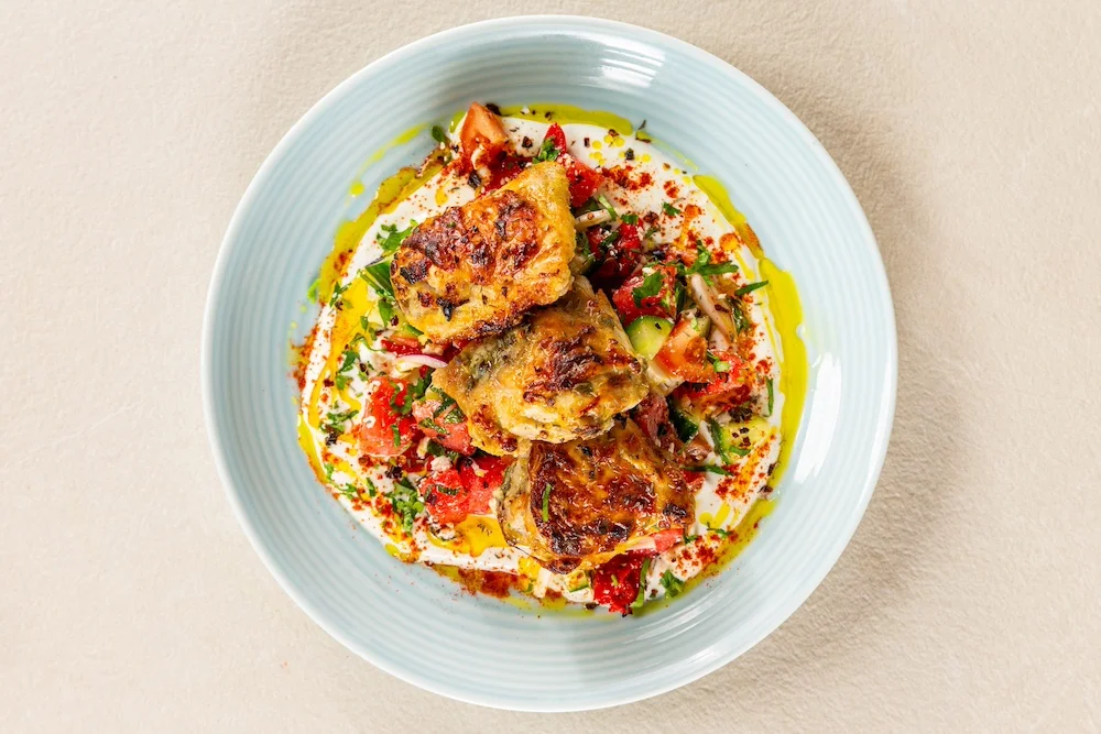 Greek yoghurt in a bowl topped with tomato, mint and cucumber salsa, crispy chicken thighs and a drizzle of olive oil.