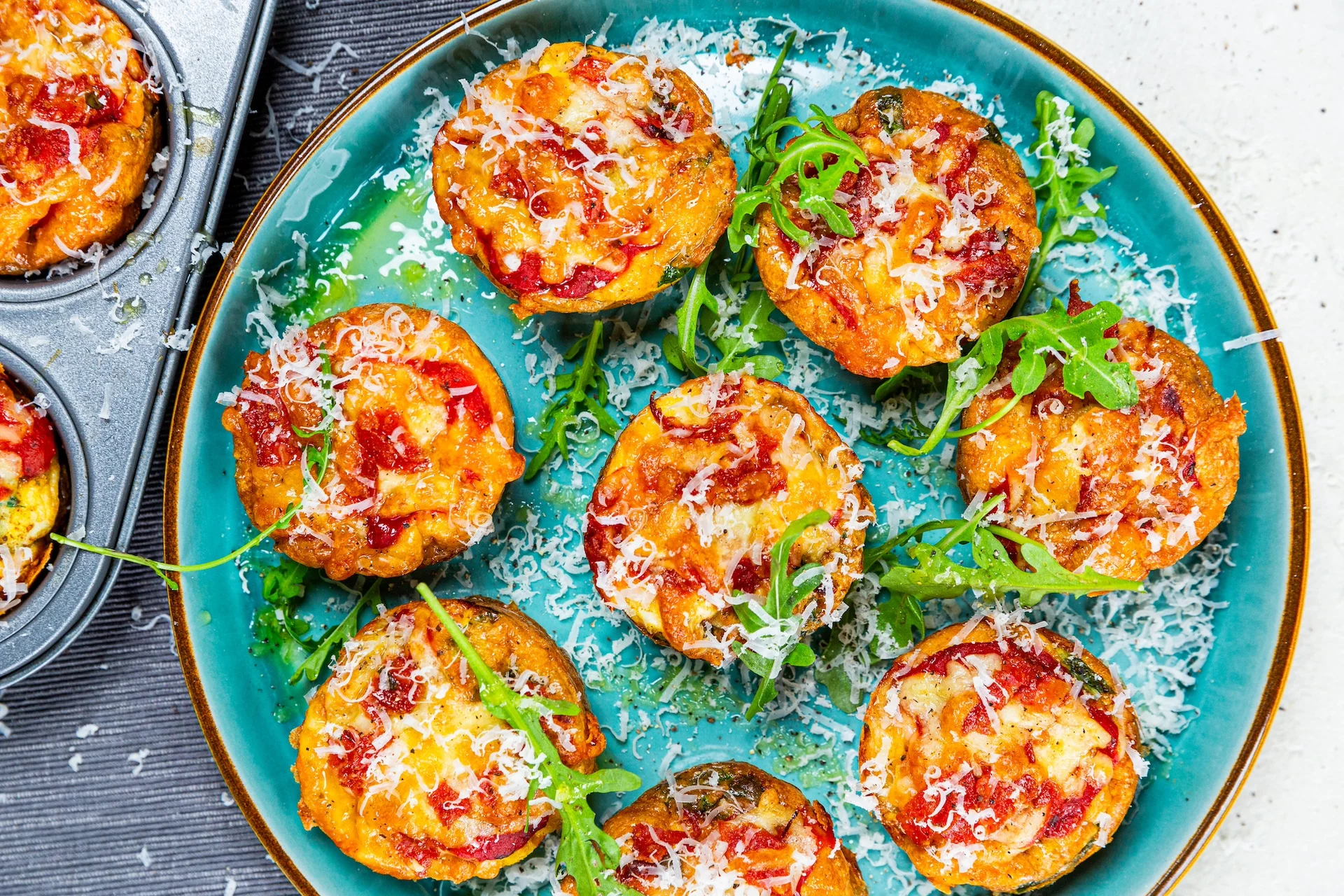 Pizza egg cups topped with grated cheese and rocket
