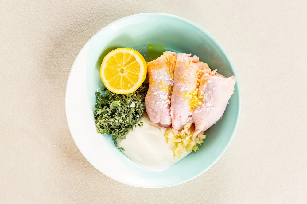 Chicken, yoghurt, chopped herbs, garlic and lemon in a bowl.